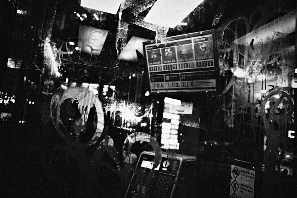Zdjęcie przykładowe z Ricoh GR IV Monochrome – nocna ulica pełna szyldów.