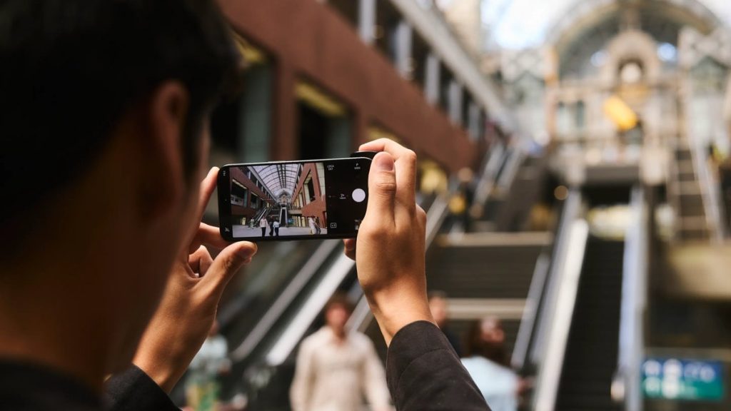 Fotograf robi zdjęcie iPhone'em z aplikacją Leica LUX w galerii handlowej