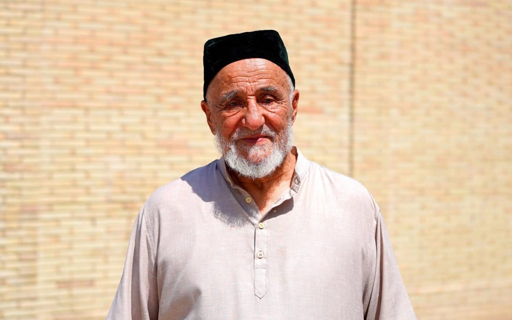 Portret starszego mężczyzny w jasnej koszuli na tle ceglanej ściany