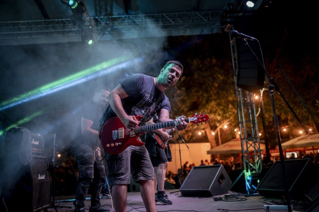 Gitarzysta z czerwoną gitarą elektryczną na scenie w zielonym świetle reflektorów i dymie