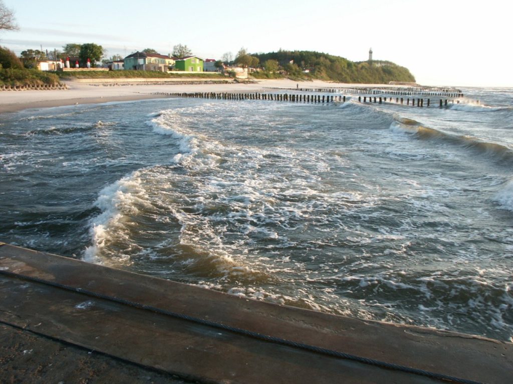 Fale sztormowe przy ostrogach na plaży w Niechorzu, w tle latarnia morska